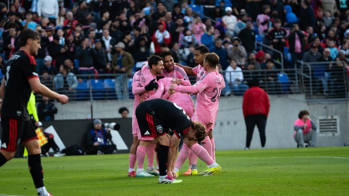 A photo of Inter Miami players celebrating a goal while D.C. United's Kye Rowles leans down to re-tie his shoes.